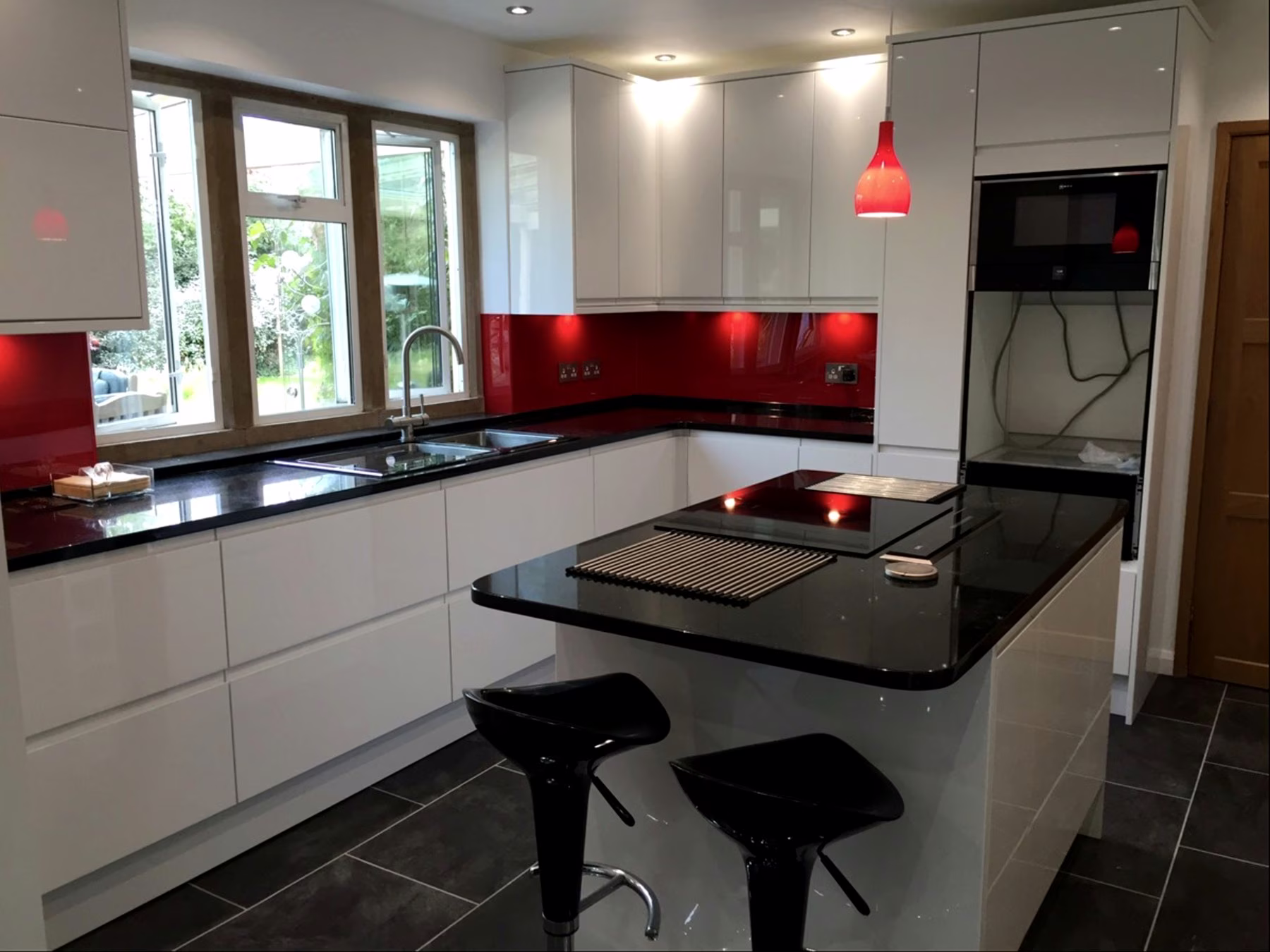 Finished kitchen with white fitted units, black worktops and red splashback