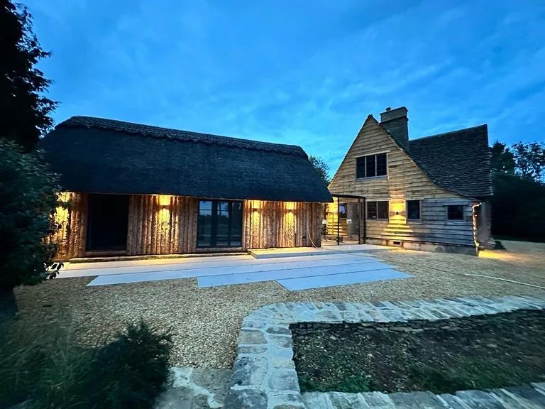 Evening view of a completed stone and timber Gloucestershire extension with warm interior lighting